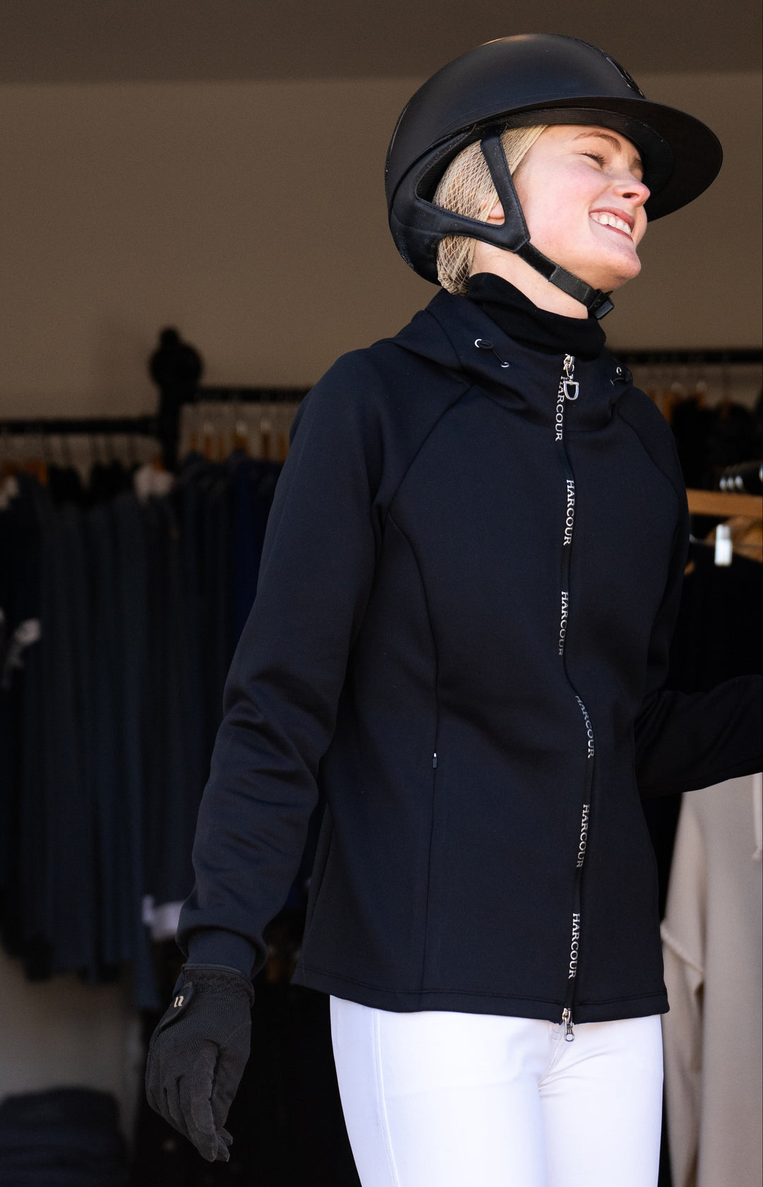Person wearing a black equestrian jacket and helmet in an indoor setting.